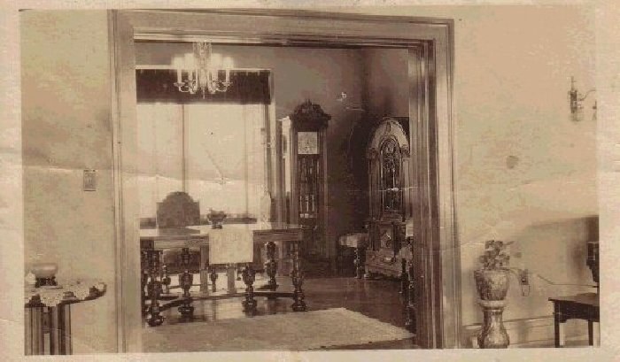 Formal parlor of Glancy Manor, mid-twentieth century interior view with grandfather clock, chandelier, and ornate cabinetry