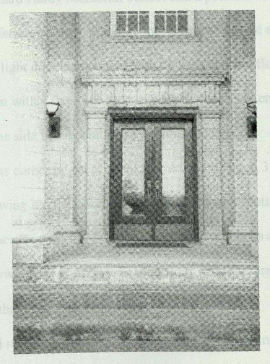 Left entrance to the school, with solid oak double doors under a rectangular glass transom and a globe lantern
