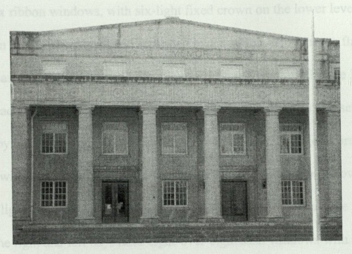 Pedimented parapet rising above the portico entrance, with bulls-eye frieze and the carved building name